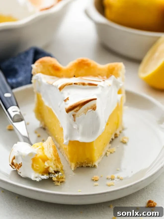A close-up shot of a fork taking a bite from a slice of lemon meringue pie, highlighting the layers of crust, filling, and meringue.