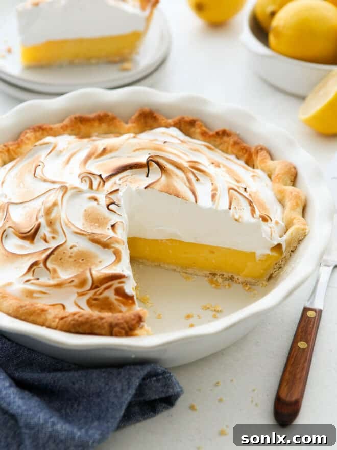 A close-up of a lemon meringue pie with a slice carefully removed, revealing the creamy filling and crisp crust.