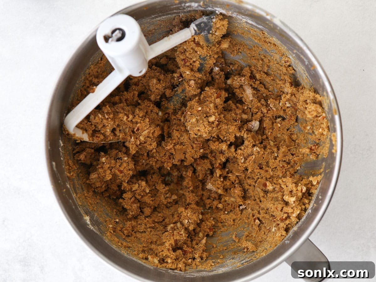 A close-up view of the rich, brown molasses spice snowball cookie dough, studded with finely chopped nuts, resting in a glass mixing bowl, ready to be portioned.