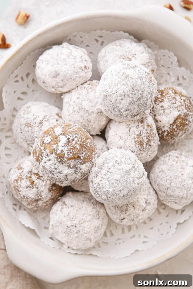 A rustic wooden bowl brimming with beautifully arranged, perfectly round Molasses Spice Snowball Cookies, generously coated in white powdered sugar, ready for serving.
