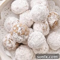 A full bowl of Molasses Spice Snowball Cookies, perfectly round and coated in powdered sugar, ready to be enjoyed.