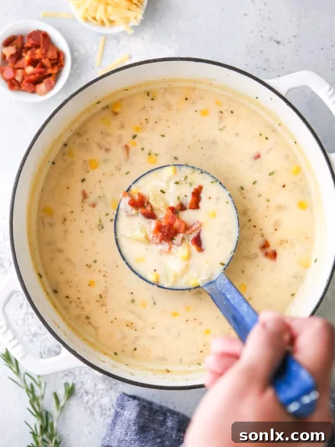 A ladle serving creamy cheesy corn chowder from a large pot, showing the rich texture and chunks of vegetables.