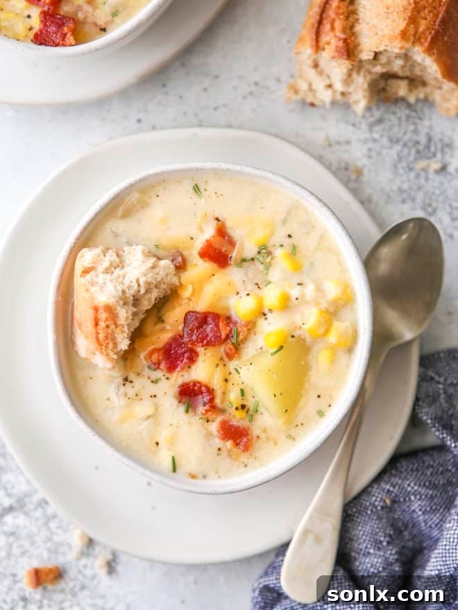 Close-up of creamy cheesy corn chowder in a bowl, with a piece of baguette on the side, highlighting its rich texture.