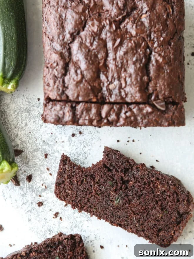 A delectable slice of chocolate zucchini bread, with a bite taken out to reveal its moist, dark crumb and melted chocolate chunks. Perfect for a summer treat.
