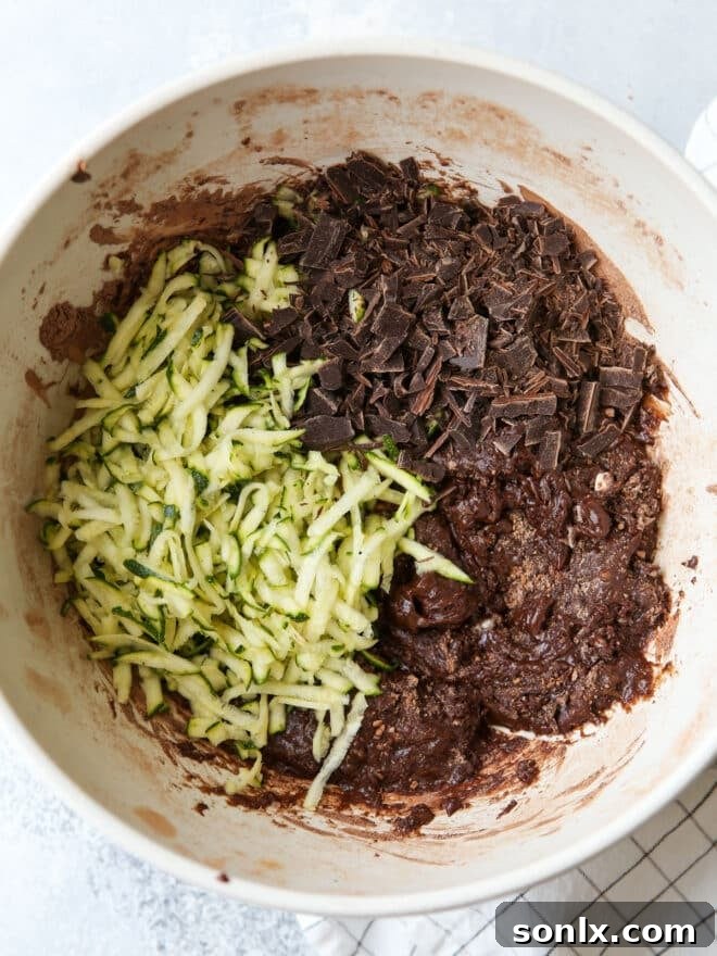 Close-up of a rich chocolate zucchini bread batter being gently folded with a spatula in a large mixing bowl.