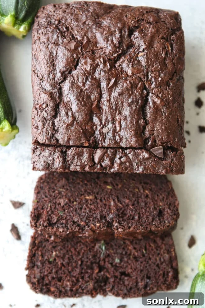 A freshly sliced loaf of chocolate zucchini bread, perfectly cut to reveal its rich, dark color, abundant chocolate chunks, and incredibly moist interior.