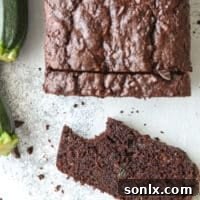 A close-up of a slice of chocolate zucchini bread with a bite taken out, showing the moist crumb and chocolate chunks.