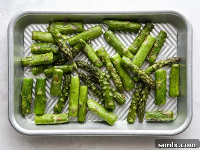 Chopped asparagus roasting on a sheet pan, showing a slightly golden and tender appearance.