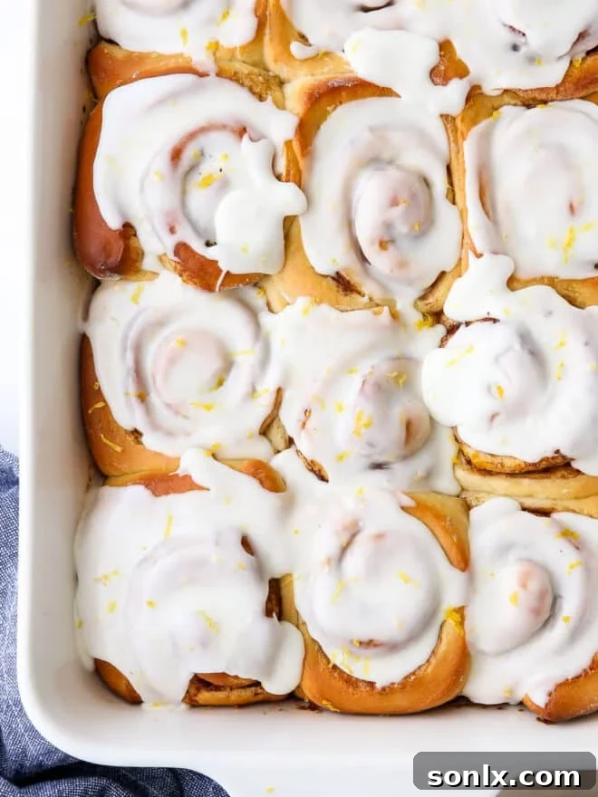 Close-up shot of glossy, glazed lemon cinnamon rolls in a pan, highlighting their soft texture and bright icing