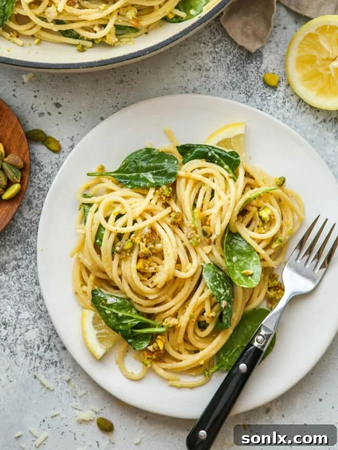 A serving of lemon pistachio pasta with spinach on a white plate, ready to be enjoyed with a fork.