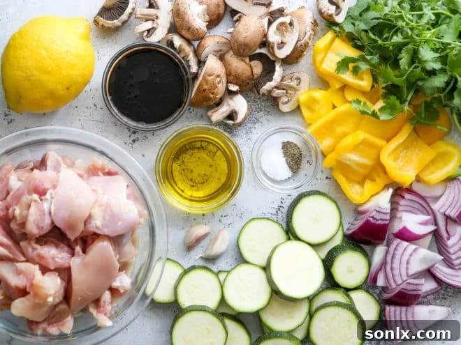 A vibrant display of fresh ingredients for grilled lemon-cilantro chicken and veggie skewers, including cubed chicken, colorful bell peppers, zucchini, mushrooms, sliced lemons, and a bunch of fresh cilantro