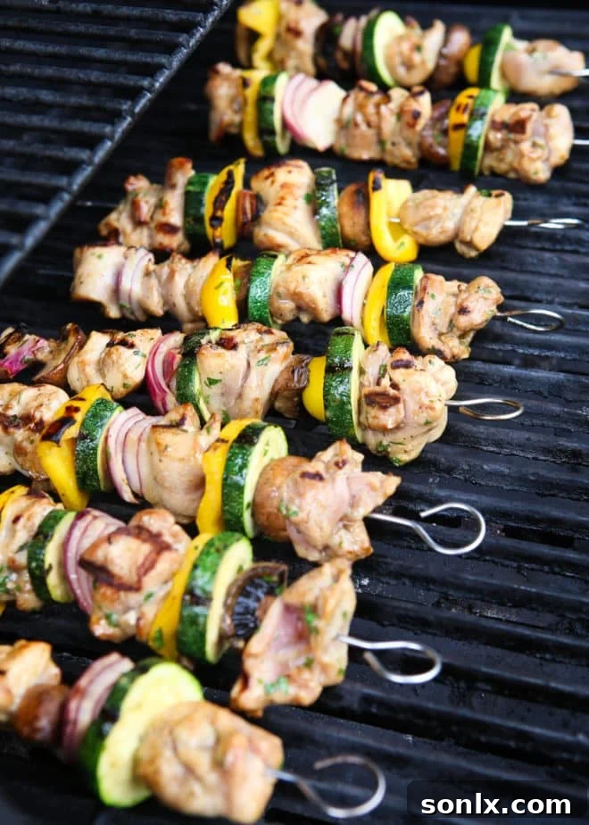Close-up view of lemon-cilantro chicken and colorful vegetable skewers cooking on a hot outdoor grill, showing appealing char marks and smoke