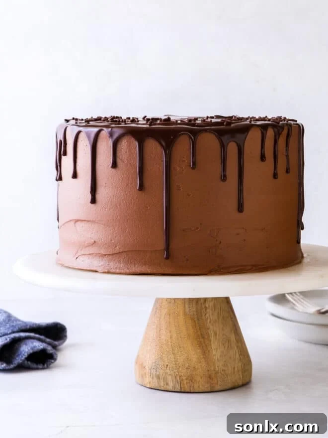 chocolate fudge layer cake on a cake stand, decorated with chocolate ganache drip