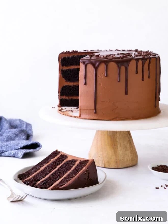 slice of chocolate fudge cake on a plate with the whole cake blurred in the background
