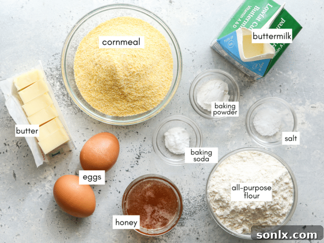 A collection of fresh ingredients laid out on a kitchen counter, including flour, cornmeal, buttermilk, honey, butter, and eggs, all ready for making honey buttermilk cornbread.