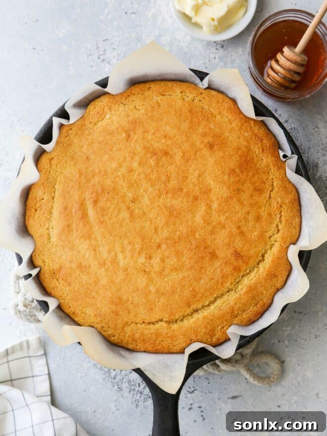 A freshly baked, golden honey buttermilk cornbread in a cast iron skillet, glistening with a perfect crust.