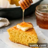 Drizzling honey onto a warm slice of honey buttermilk cornbread, emphasizing its sweet and moist appeal.