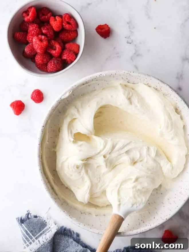 Bowl of creamy white chocolate buttercream frosting next to a bowl of vibrant fresh raspberries