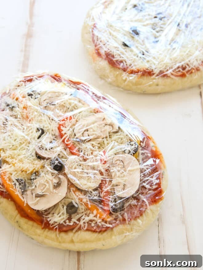 Homemade pizzas meticulously wrapped in plastic wrap, stacked and ready for long-term storage in the freezer.