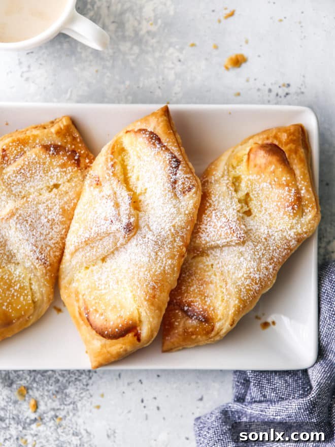 A plate stacked with freshly baked cream cheese Danishes, dusted with powdered sugar, ready to be enjoyed.