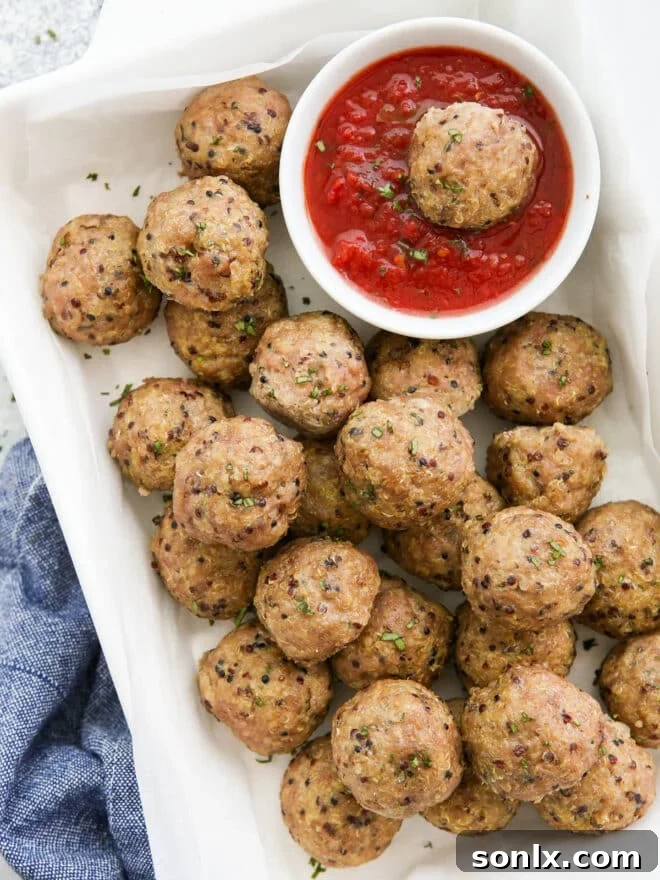 Delicious baked pork quinoa meatballs served with a bowl of rich marinara sauce, garnished with fresh basil.