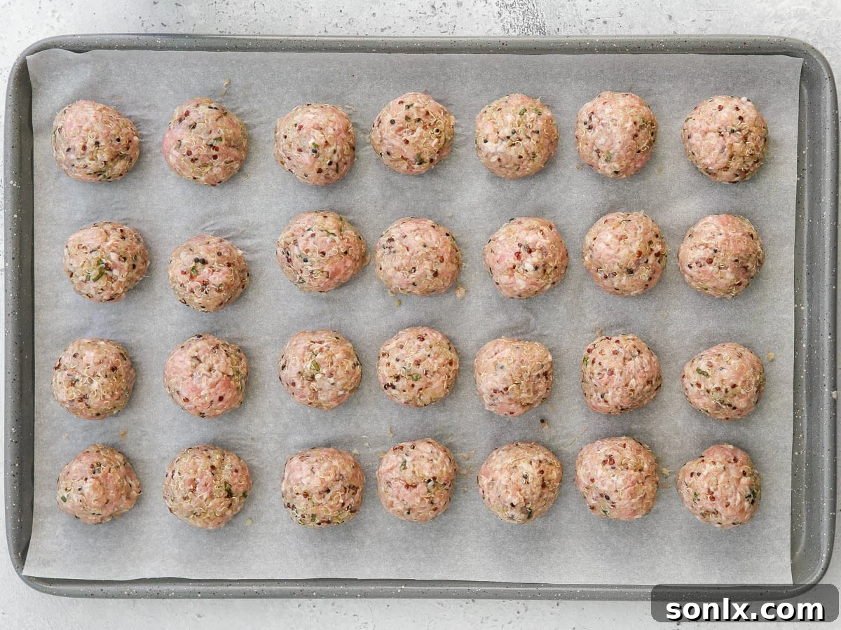 Scooped and rolled pork quinoa meatballs neatly arranged on a parchment-lined baking sheet, ready for baking.