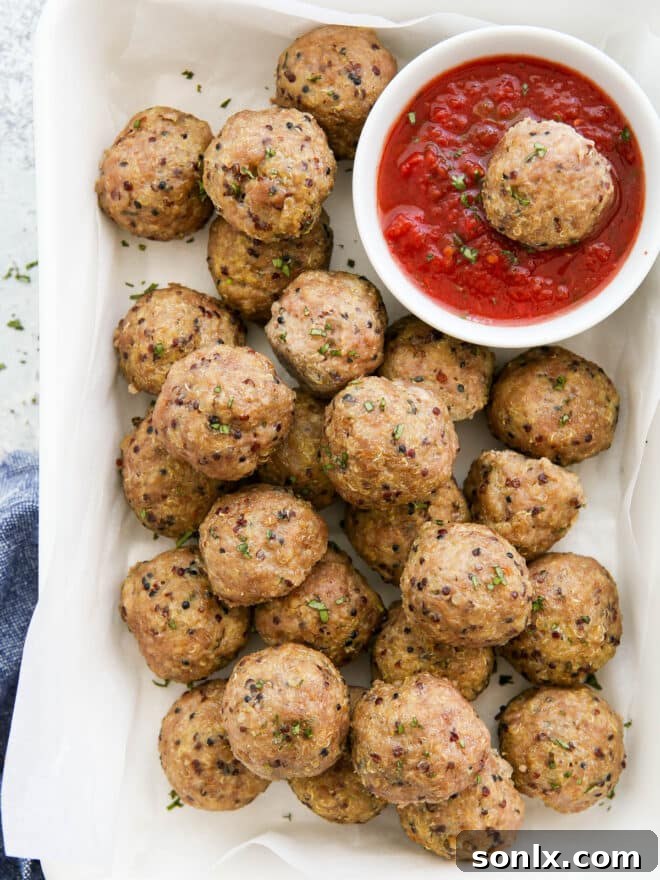 Close-up of two perfect pork quinoa meatballs served on a plate with fresh basil, next to a bowl of marinara sauce.