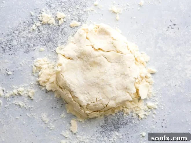 A ball of homemade buttermilk pie dough being gently shaped into a flat disk on a lightly floured surface, ready for chilling.