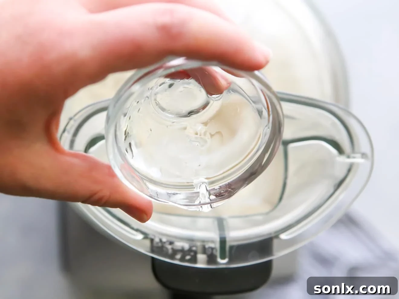 Ice-cold water being poured into a food processor while it's running with flour and butter mixture.
