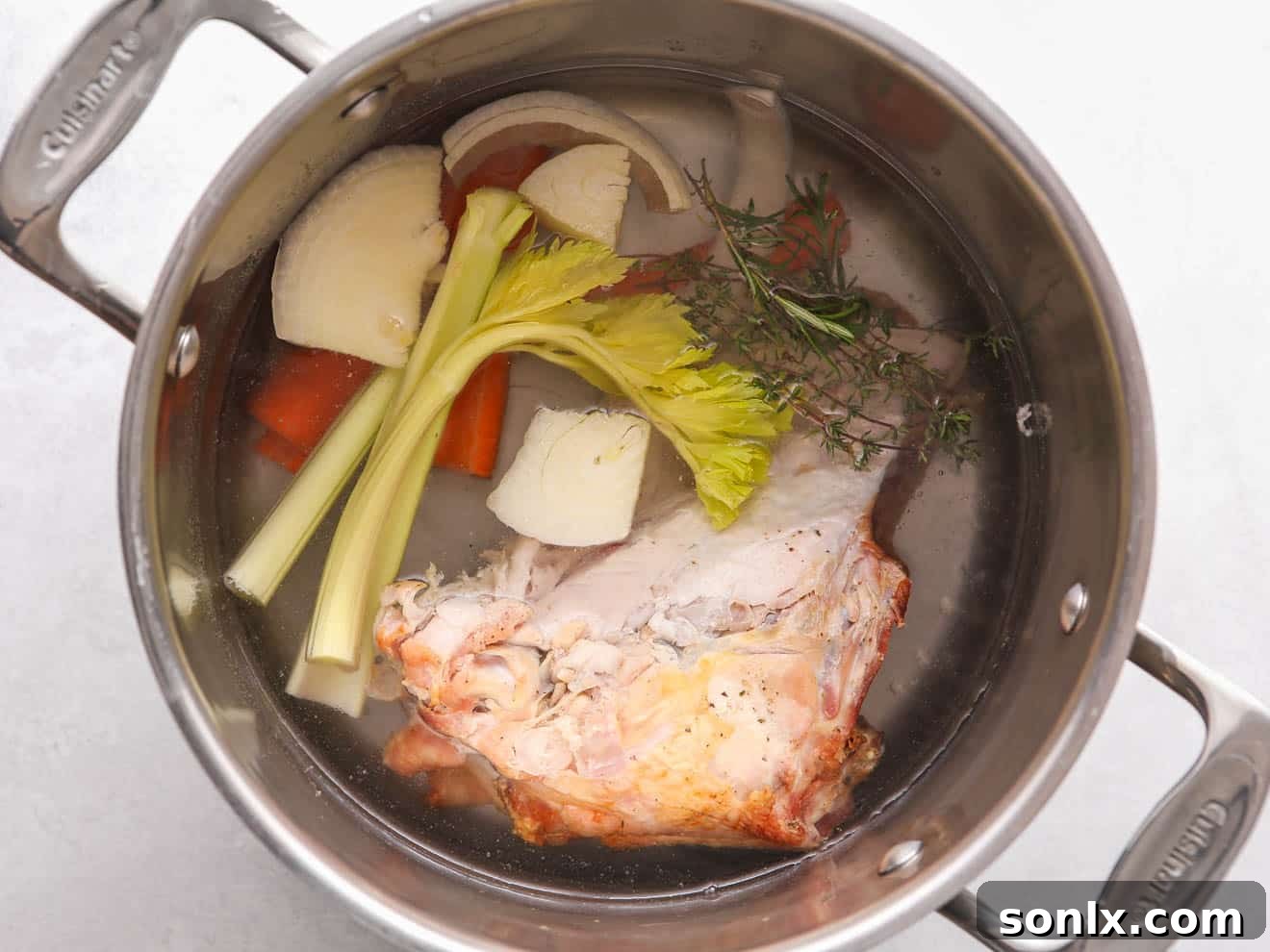 Turkey bones and fresh vegetables like carrots, onions, and celery being added to a large pot, ready for broth making.
