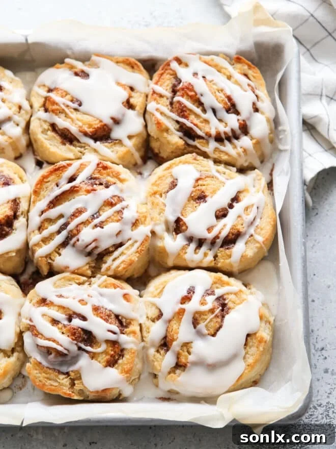 Baked cinnamon roll biscuits, golden brown and drizzled with icing, in a baking pan, ready to be enjoyed.