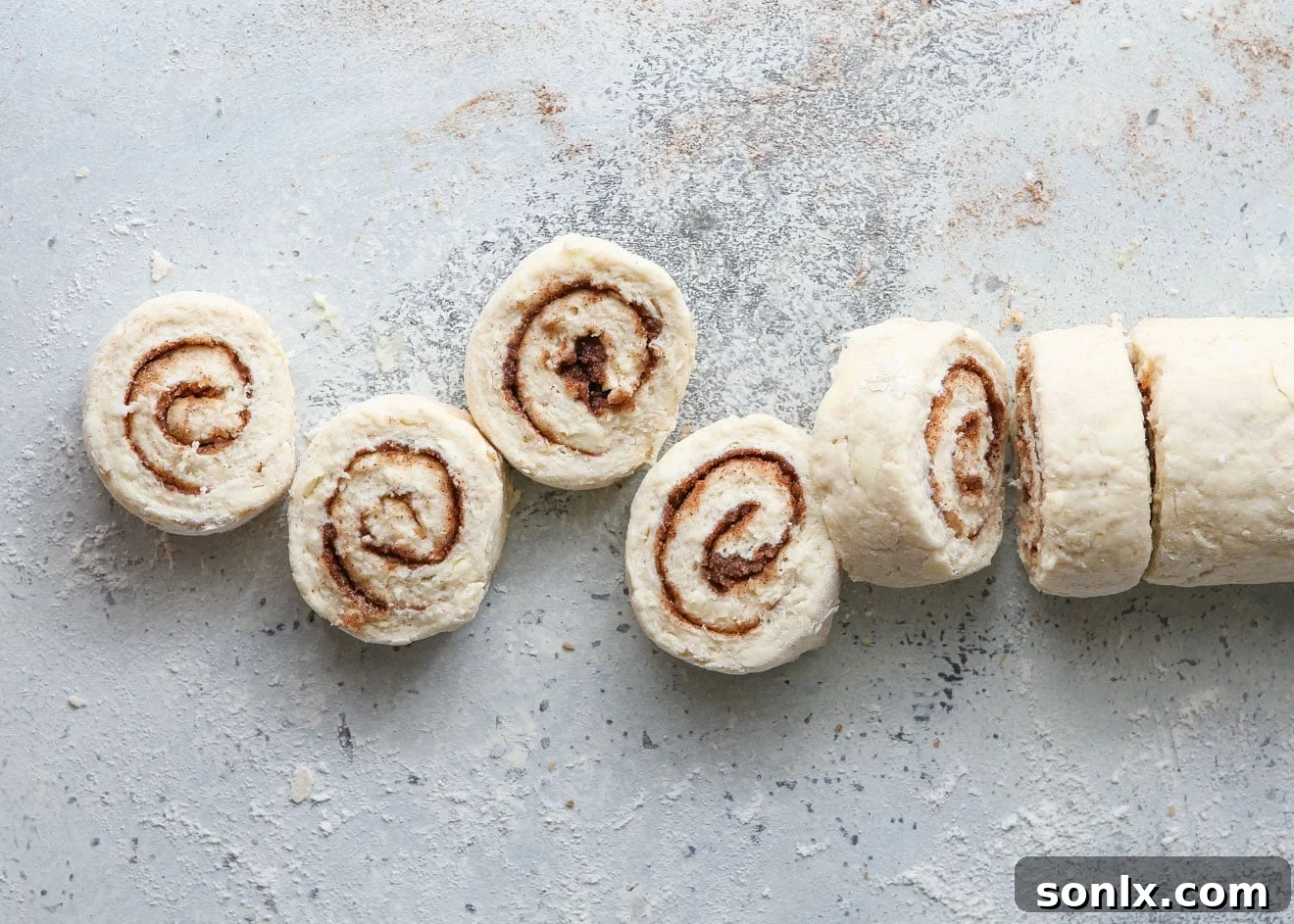 Close-up of sliced cinnamon roll biscuit rounds neatly arranged on a baking sheet, ready for baking.