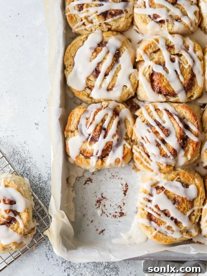 A pan of baked cinnamon roll biscuits, with one missing, showing the tempting icing drizzle and golden crust.