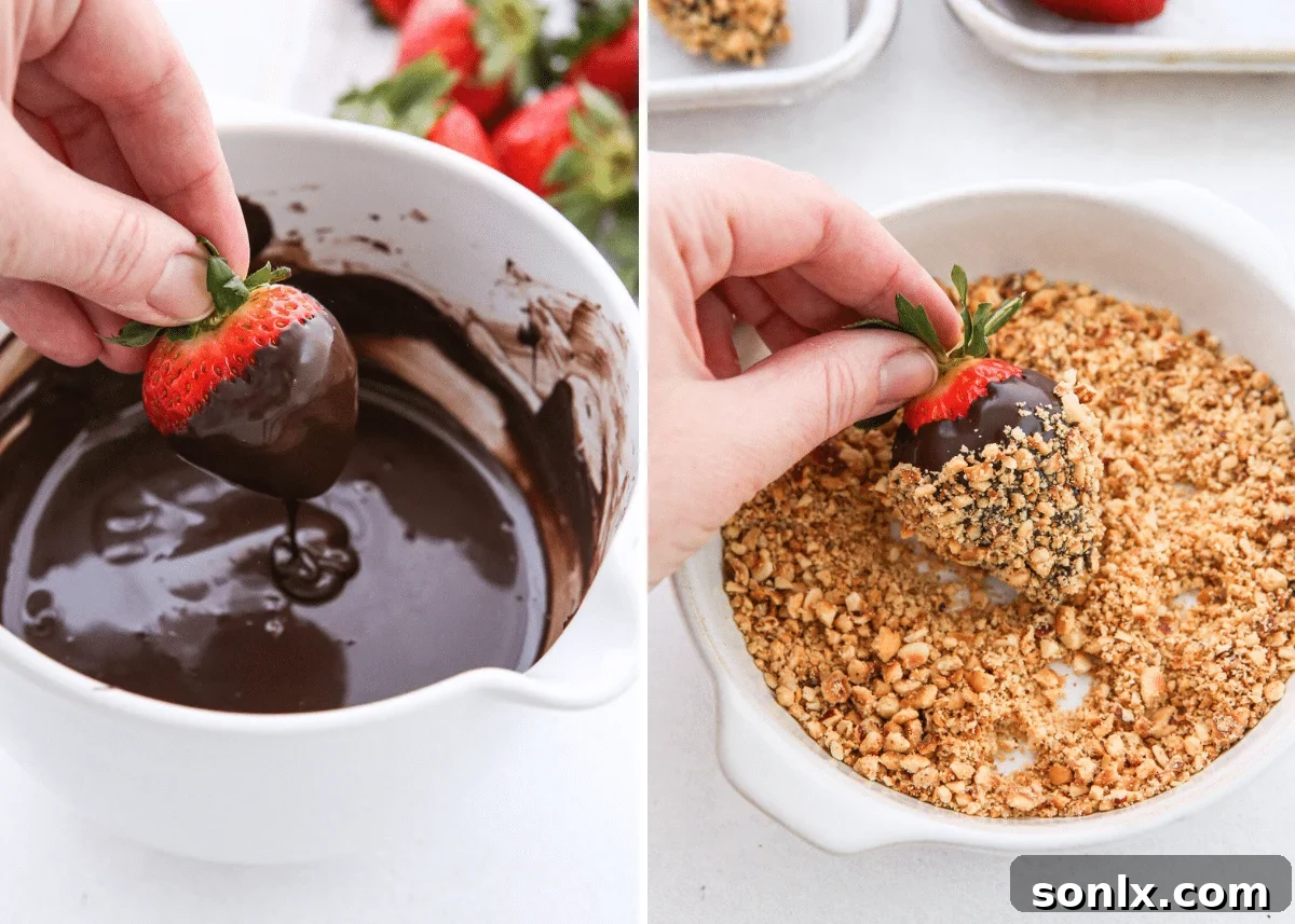 A hand dipping a strawberry into melted chocolate, with another strawberry being rolled in chopped hazelnuts.