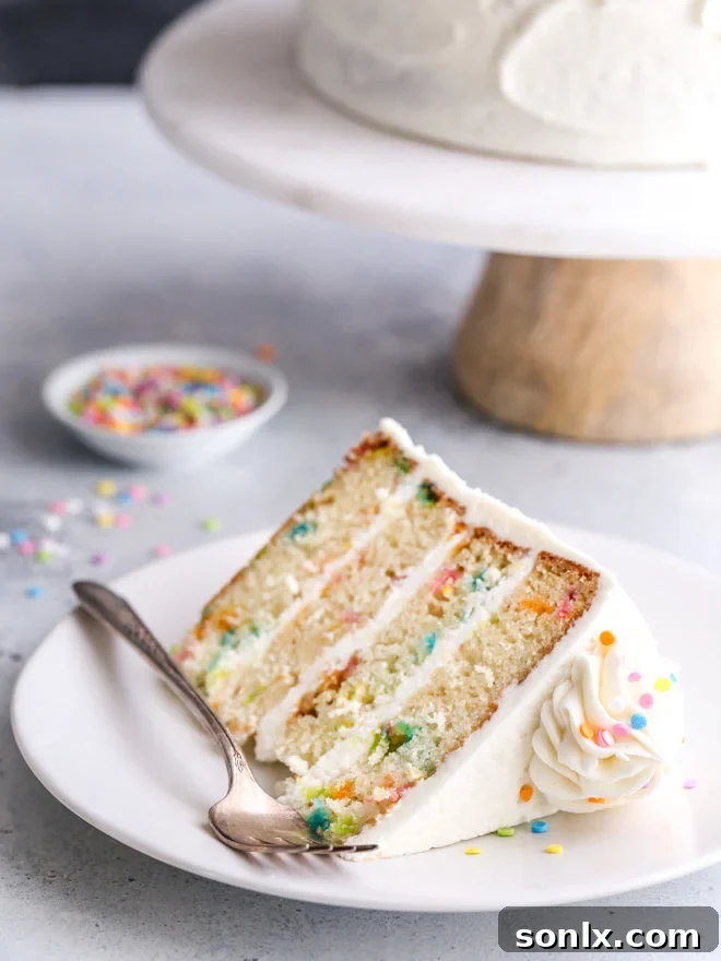 A close-up of a slice of funfetti cake, showing its moist texture, colorful sprinkles, and rich vanilla buttercream.
