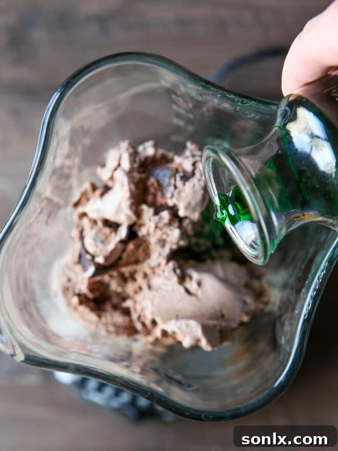 Pouring crème de menthe liqueur into a blender with chocolate ice cream