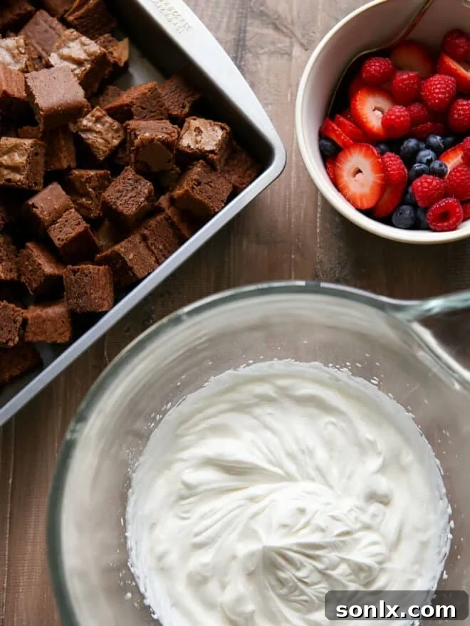 Berry Brownie Bliss Trifle 4 Ingredients for brownie berry trifle laid out: cubed brownies, freshly whipped cream, and a medley of colorful fresh berries.