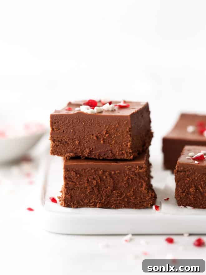 A generous stack of glossy, dark chocolate peppermint fudge squares, perfectly cut and arranged on a simple white plate, ready to be enjoyed.
