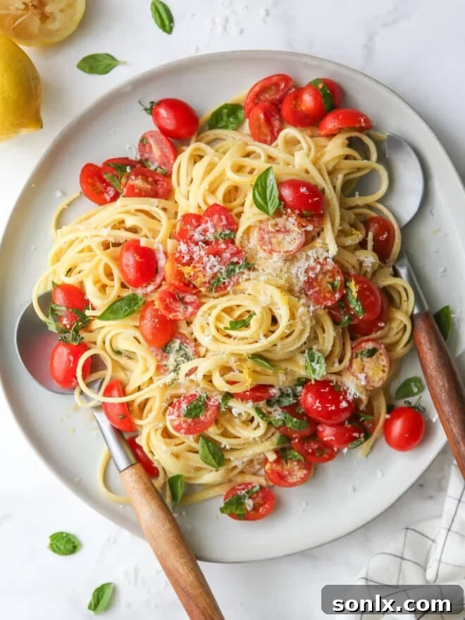 Delightful lemon pasta with cherry tomatoes and fresh basil on a white plate with cutlery, ready to be enjoyed.