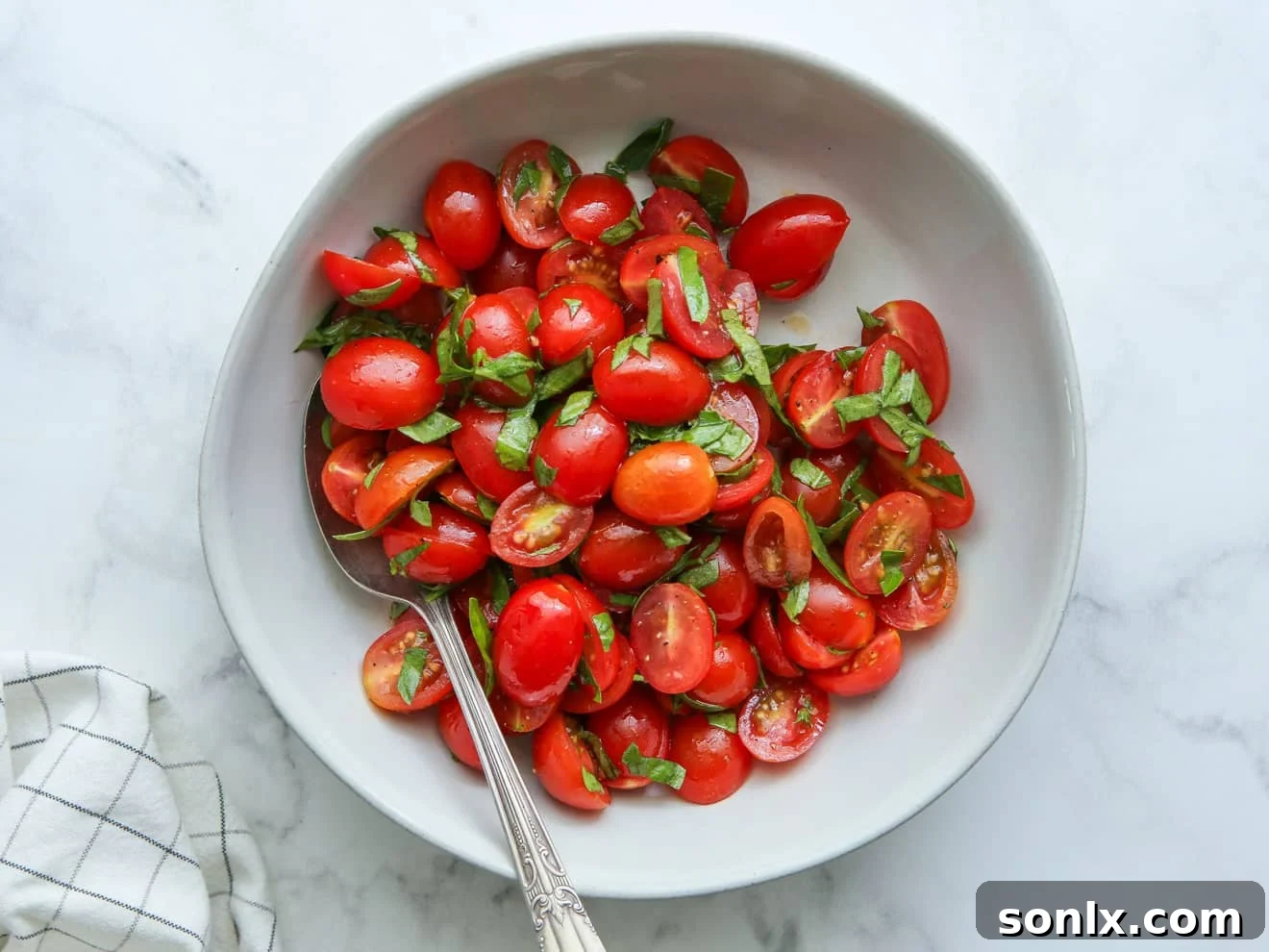 Fresh cherry tomatoes and basil being tossed with olive oil, salt, and pepper in a bowl, ready for marination.