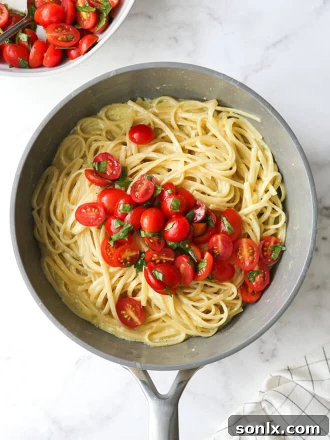 Folding marinated cherry tomatoes and fresh basil into a pot of lemon pasta, creating a vibrant and flavorful dish.