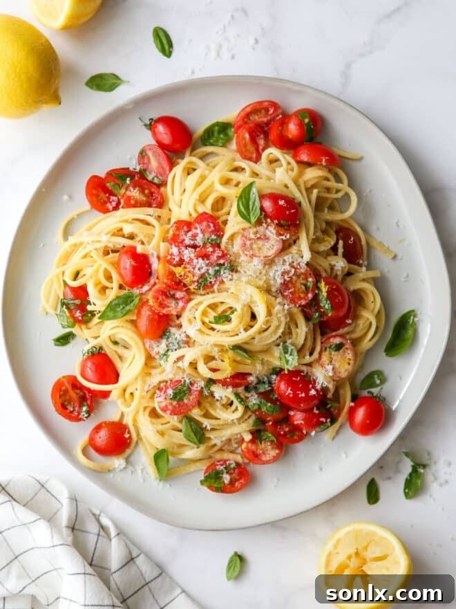 Close-up of creamy lemon pasta with tomatoes and basil on a white plate, garnished with fresh basil leaves.