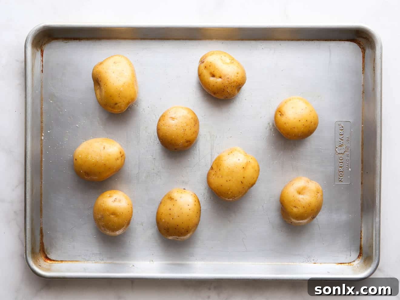 Small gold potatoes arranged on a baking sheet, ready for roasting.