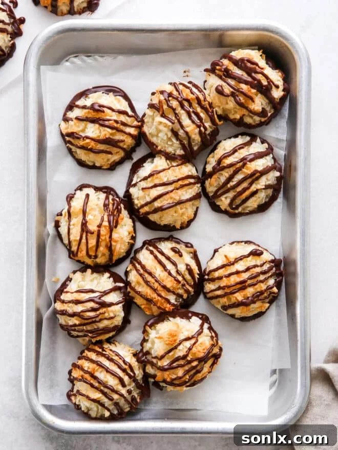 Golden-brown coconut macaroons, some elegantly drizzled with dark chocolate, arranged on a parchment-lined sheet pan, ready for serving.