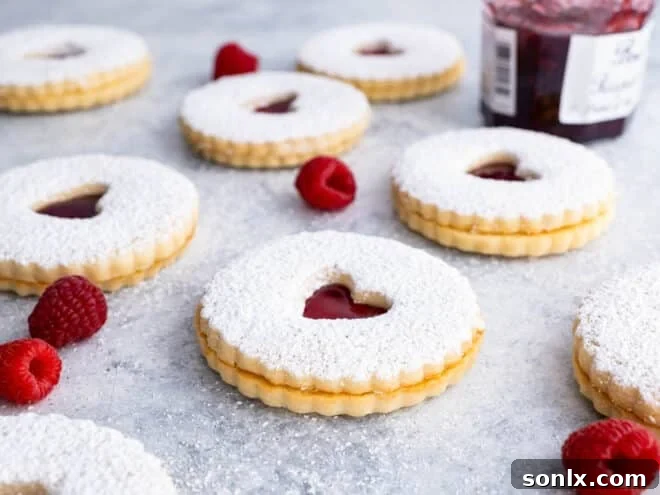 Beautifully baked Raspberry Almond Linzer Cookies, dusted with powdered sugar and filled with jam.
