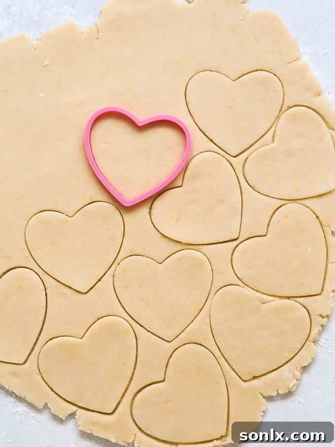 Process of rolling out cookie dough and using cookie cutters to create heart shapes for Linzer cookies, with smaller cut-outs for the jam windows.