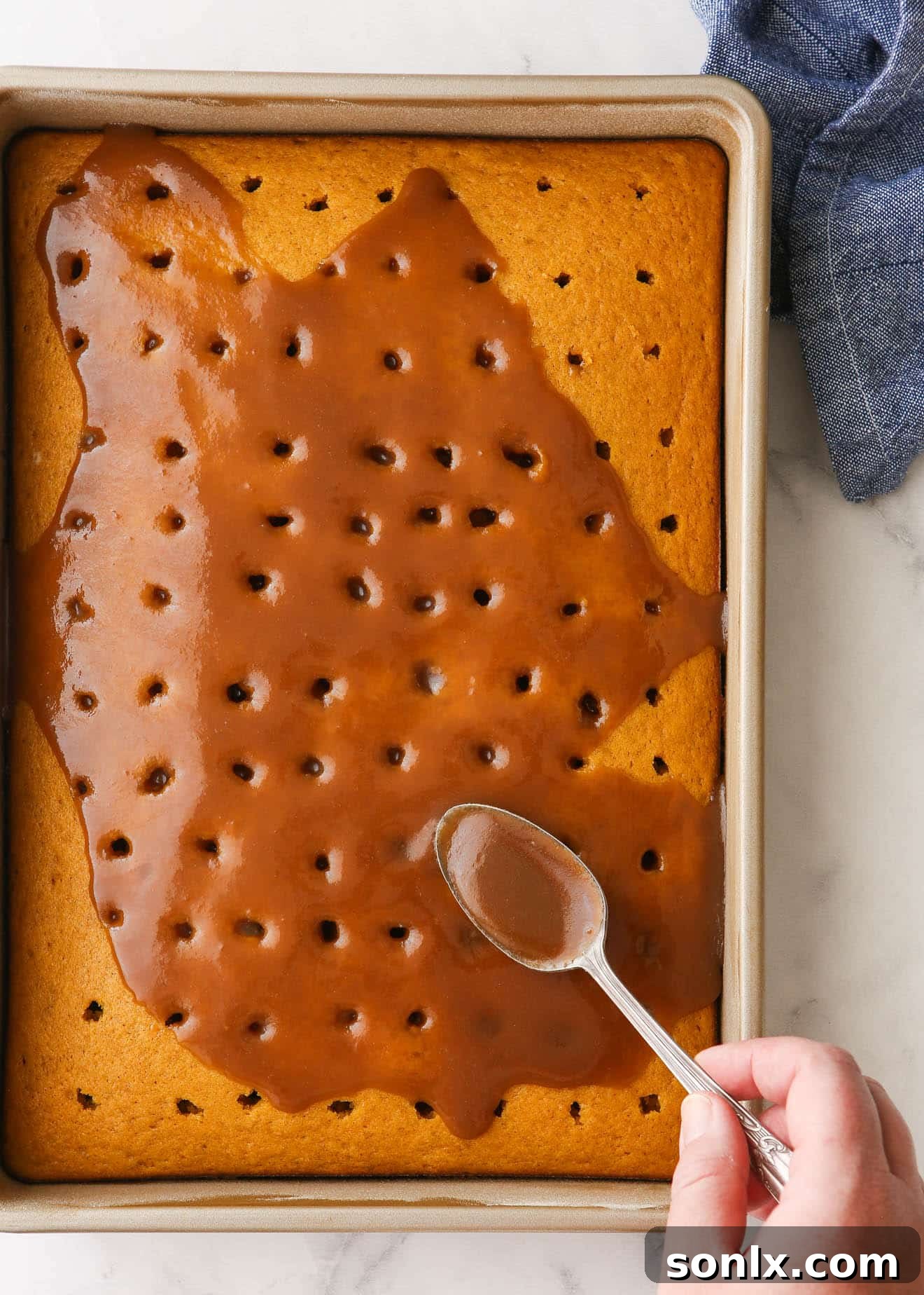 Warm caramel sauce being gently poured over a pumpkin cake with an array of holes, ensuring the sweet liquid soaks deeply into every part.