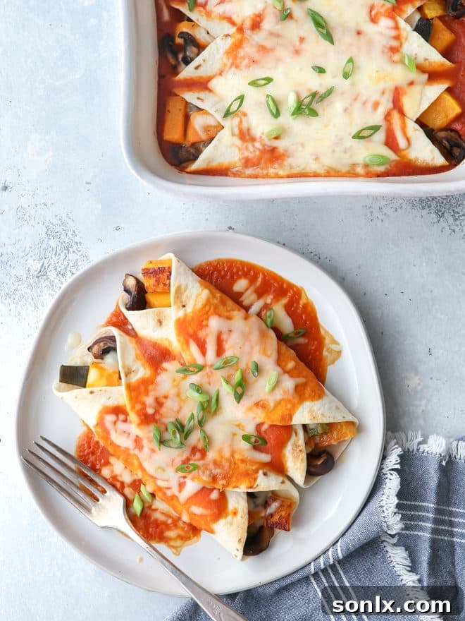 A close-up shot of golden-brown butternut squash enchiladas, topped with melted cheese and fresh cilantro.