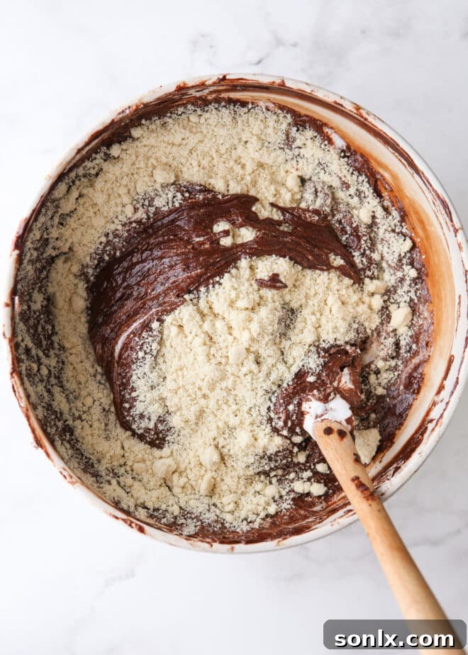 Flour Power: The Science Behind Perfect Baking 7 A baker gently folding fine almond flour into a rich chocolate cake batter, highlighting the texture difference