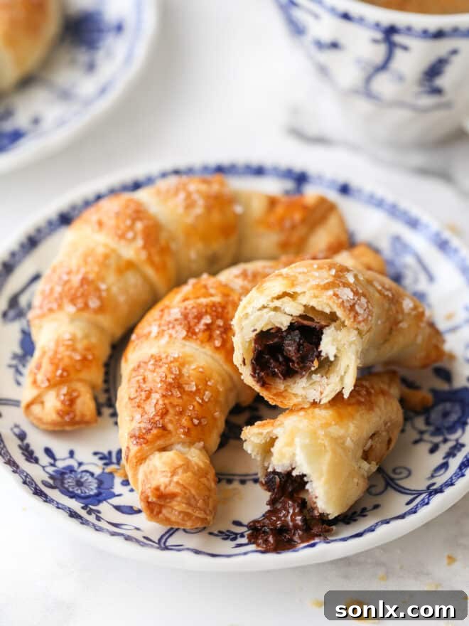Close-up view of two freshly baked puff pastry chocolate croissants on a plate, showing the flaky layers and melted chocolate